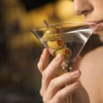 Close up of mid adult Caucasian woman drinking a martini with three olives.