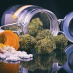 Detail of cannabis buds and prescriptions pills over reflective surface - medical marijuana dispensary