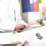 Patient holding paper document, insurance, bill or invoice with dollar sign in doctor office in hospital or emergency room.