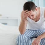 man sitting on the edge of a bed and feeling sick from the symptoms of drug withdrawal