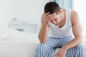 man sitting on the edge of a bed and feeling sick from the symptoms of drug withdrawal