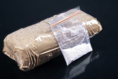 A clear bag of powder cocaine leaning against a brick of cocaine 